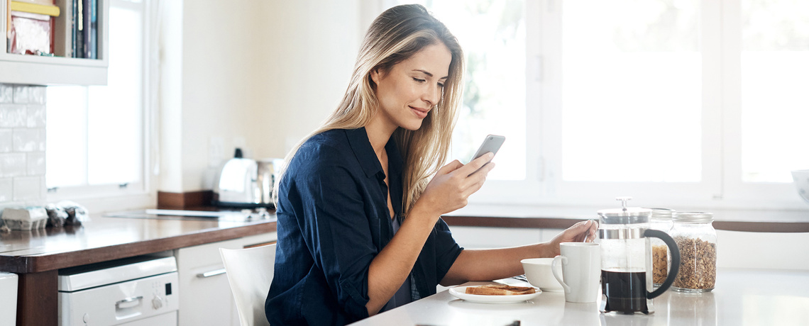 Frau mit Smartphone am Frühstückstisch liest DigitalBasis der NNN